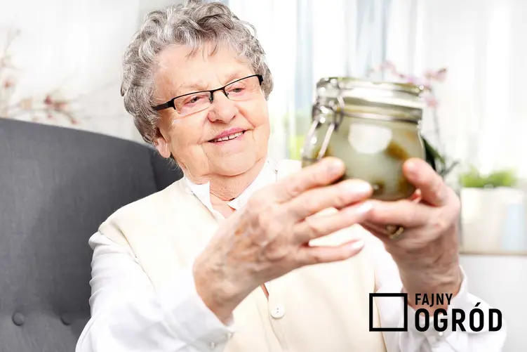 Starsza pani trzymająca słoik ogórków, a także sok z kiszonych ogórków, jego właściwości lecznicze i wpływ na zdrowie układu pokarmowego