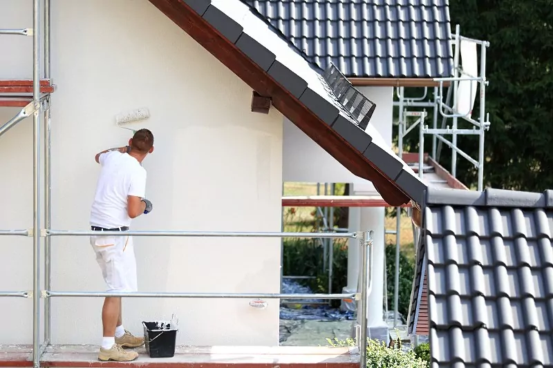 mężczyzna malujący elewację na jasny kolor